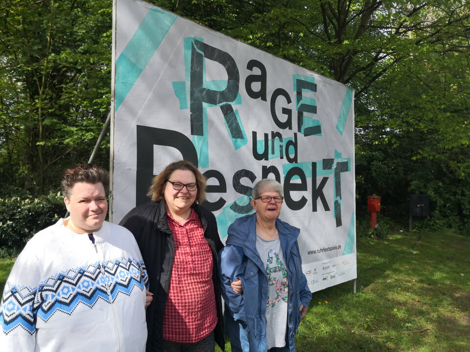 3 Personen vor einem Plakat