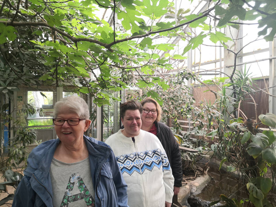 Drei Personen gehen durch einen großen Raum mit Pflanzen.