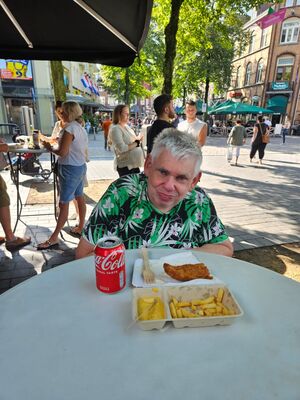 Ein Mann sitzt an einem Tisch darauf stehen Fisch, Pommes und Cola.