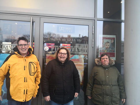 Drei Personen vor dem Eingang eines Kinos.