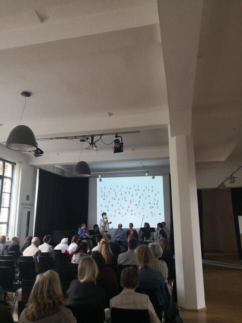 Ein Raum voller Menschen hört einer Sprecherin zu.
