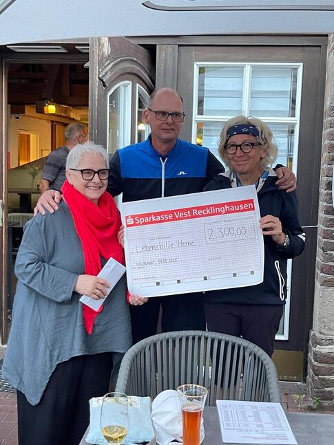 Zwei Frauen mit einem Mann halten einen Scheck in der Hand. Der Mann umarmt die beiden Frauen.