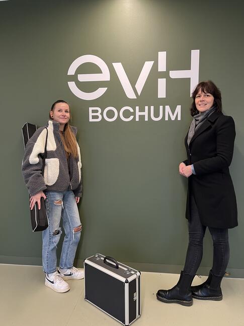 Zwei Frauen stehen vor einem Logo der evH Bochum.