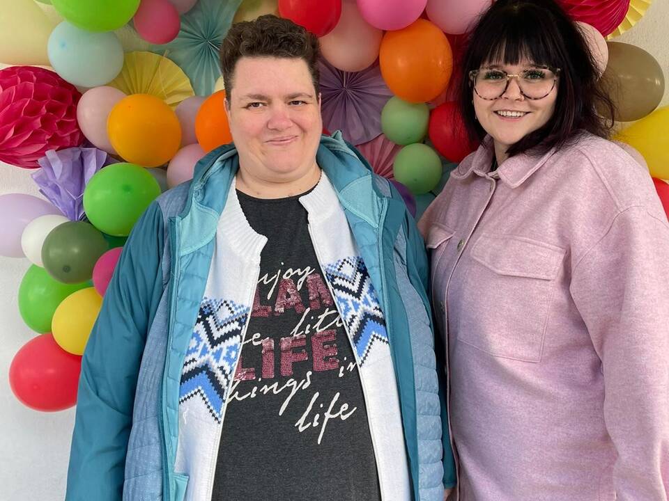 Zwei Frauen vor einer Wand mit bunten Luftballons.